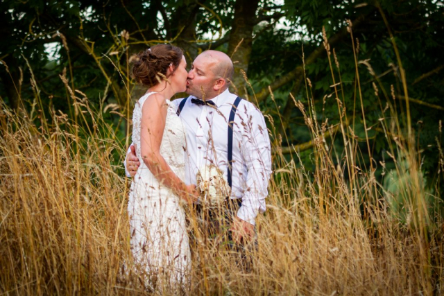 Bride an groom kissing in field of straw at Broom Hall Saham Toney