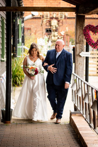 Bride being walked in to ceremony at Glebe Farm Barn NR9 4AP