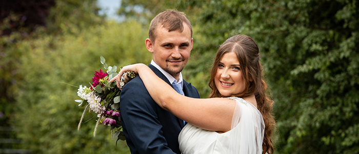 AlanBulldeathPhotographyBanner4 Bride and groom posing outside with bridal flowers at Glebe Farm Barn Norfolk